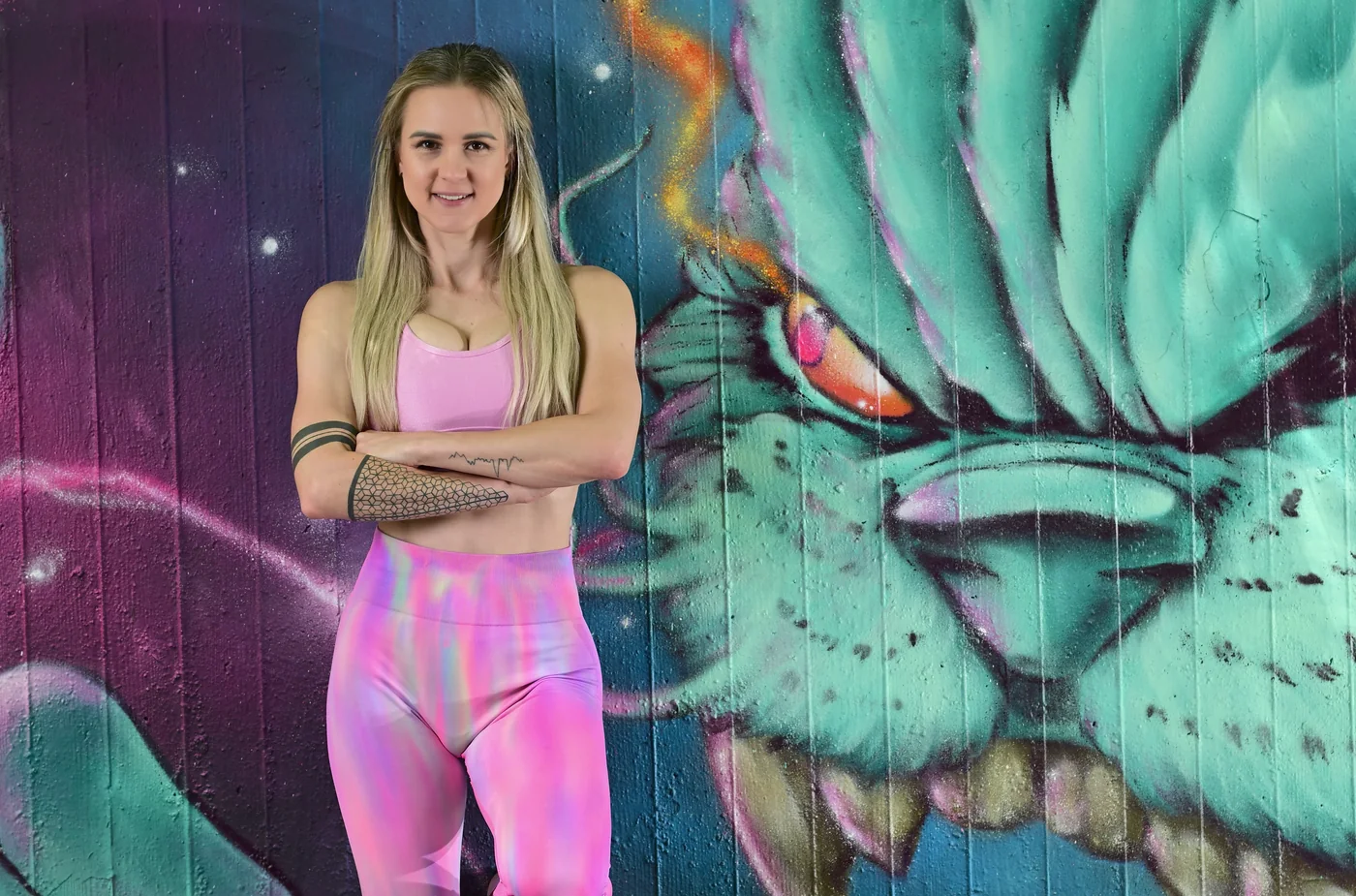 Olga standing in pink activewear in front of a colourful mural